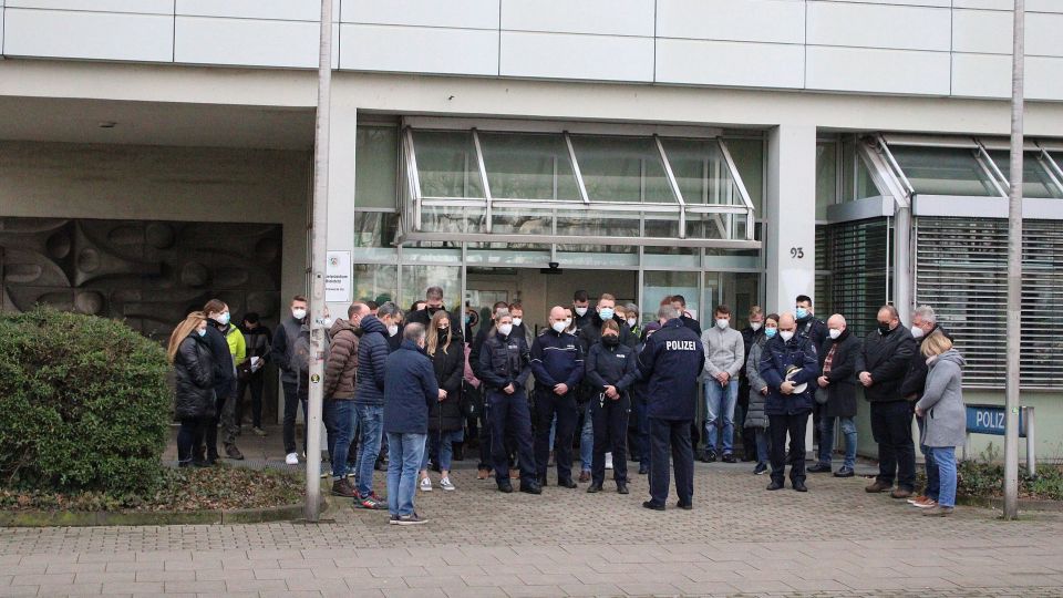 Mehrere Personen stehen zur Schweigeminute vor der Polizeiwache Ost.